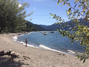 Ein Strand mit Booten, eine Person am Wasser und Berge im Hintergrund.