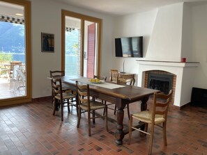 A dining area with a wooden table and chairs, a fireplace, and a television mounted on the wall. - Casa Andrea Panorama by Interhome (Gerra)