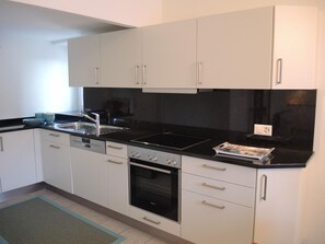 A modern kitchen with white cabinets, a black countertop, a dishwasher, an oven, and a sink. - Casa Felice by Interhome (Brissago)