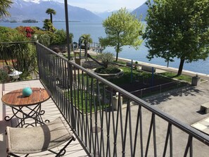 A balcony with a view of a lake and mountains, a small garden, and a table with a chair. - Casa Felice by Interhome (Brissago)