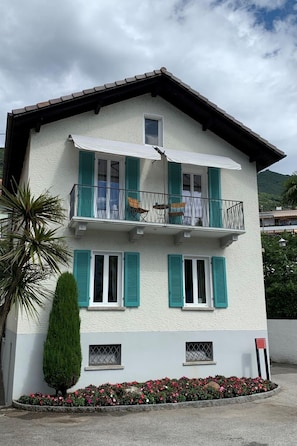 Un immeuble de deux étages doté d’un balcon, d’une façade blanche et de volets verts.