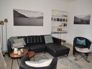 A modern living room with a black leather sectional sofa, a small round coffee table, a black armchair, and a bookshelf with books and decorative items. - Casa Felice by Interhome (Brissago)