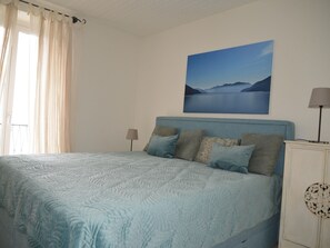 A bedroom with a bed, a nightstand, a lamp, and a painting of a landscape. - Casa Felice by Interhome (Brissago)