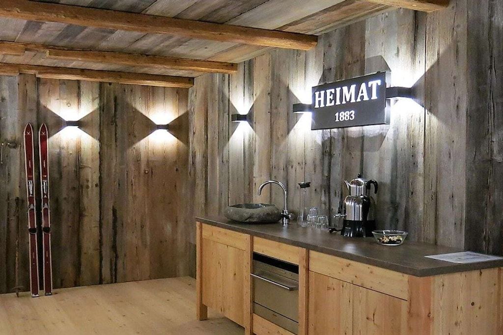 A rustic wooden interior with a sign reading 'HEIMAT 1883' and skis leaning against the wall.
