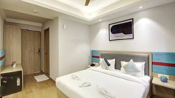 A hotel room with a bed, a ceiling fan, a framed artwork, and a wooden wardrobe.
