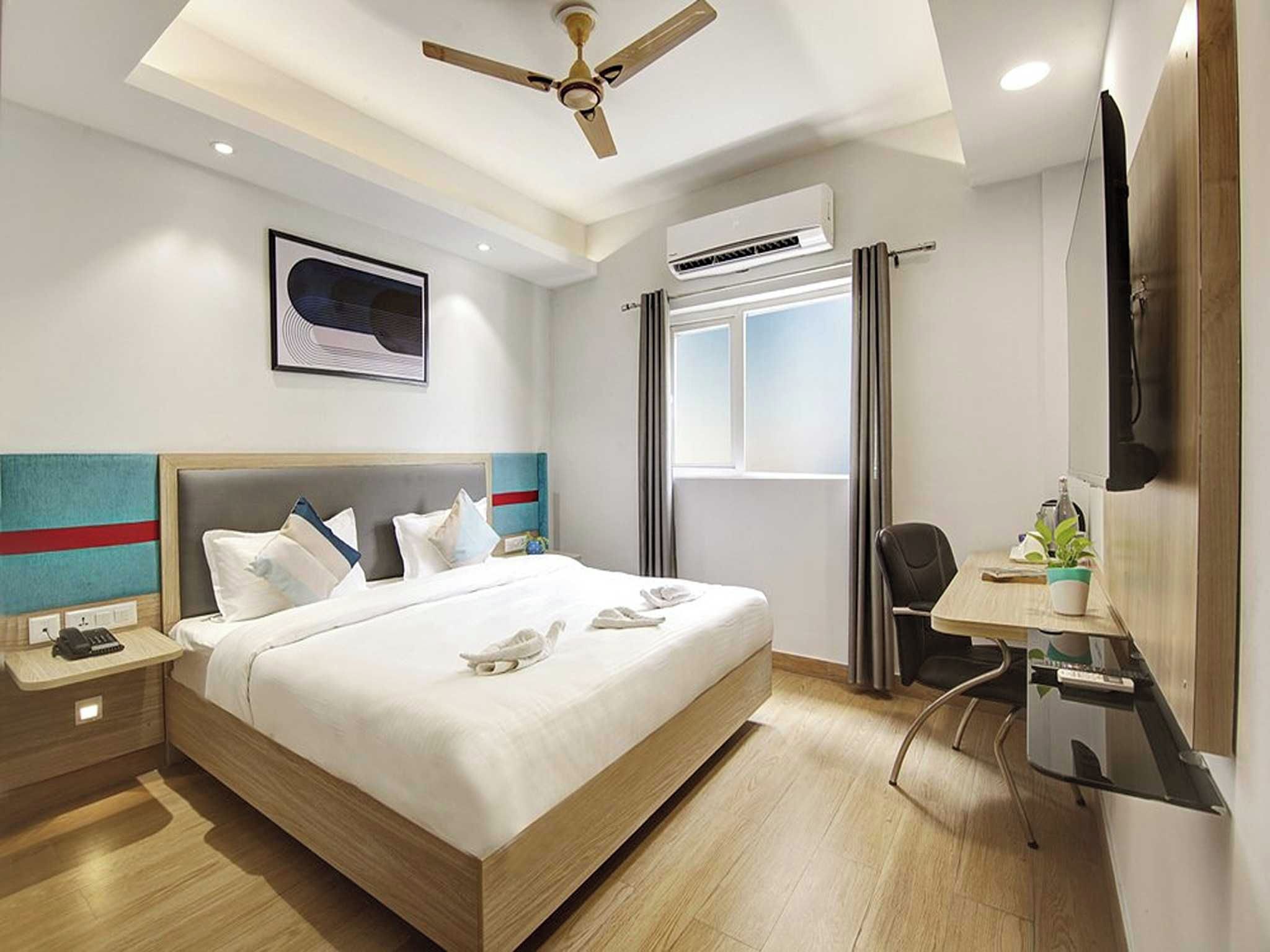 Ein Hotelzimmer mit Bett, Nachttisch, Schreibtisch, Stuhl und Deckenventilator.