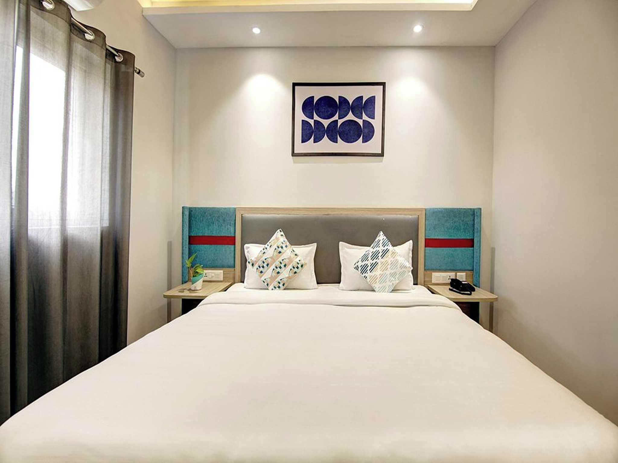 A hotel room with a large bed, two bedside tables, a nightstand, a wall-mounted artwork, and a curtain.