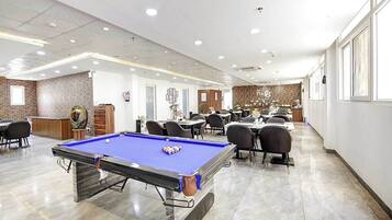 A billiards table in a well-lit room with a pool table, chairs, and a brick wall.