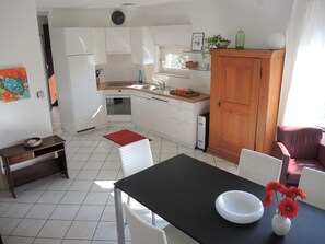 Eine kompakte Küche mit weißen Schränken, einer schwarzen Arbeitsplatte und einem Holzschrank. Es gibt einen Esstisch mit Stühlen und eine Vase mit Blumen.