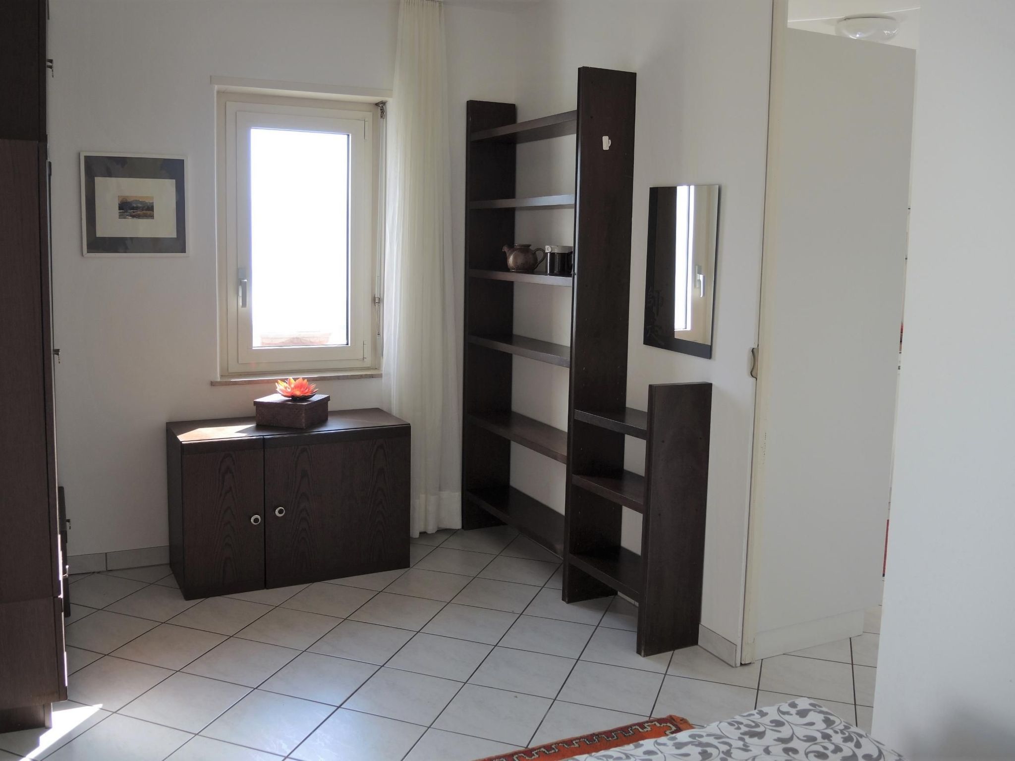 Ein Zimmer mit Fenster, Schrank, Regale und Spiegel.