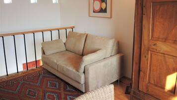 Ett vardagsrum med en beige soffa, en mönstrad matta, ett träskåp och ett trappräcke.