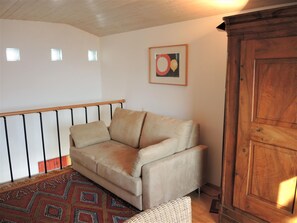 Ein Wohnzimmer mit beiger Couch, einem gemusterten Teppich, einem Holzschrank und einer Treppengeländer.
