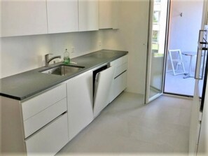 A modern kitchen with a stainless steel sink, white cabinets, and a glass door leading to a balcony. - Bellavista by Interhome (Locarno)