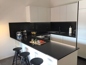 A modern kitchen with a black countertop, white cabinets, a built-in stove, and a sink. There are three black stools at the counter. - Sabrina App. 129 by Interhome (Ascona)