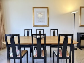 A dining area with a wooden table and six chairs, a framed artwork on the wall, and a floor lamp. - Portofino by Interhome (Brissago)