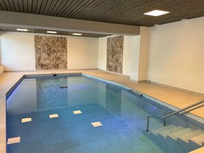 Ein Schwimmbecken mit klarem, blauen Wasser, umgeben von gefliesten Wänden und einer Holzbalkendecke.
