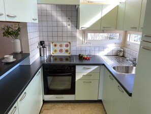 A kitchen with white cabinets, a black countertop, a built-in oven, a sink, and a window providing natural light. - Al Lido by Interhome (Locarno)