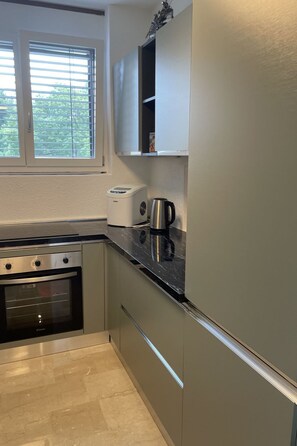 Eine Küche mit Einbauofen, Kaffeemaschine und einem Fenster mit Jalousien.