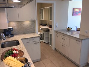 A kitchen with a sink, stove, and cabinets. There is a bowl of vegetables and a pot of pasta on the counter. - Monte Fiorito by Interhome (Orselina)