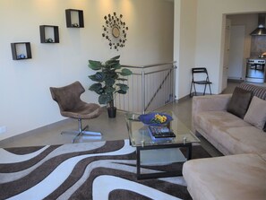 A living room with a brown chair, a glass coffee table, a beige sofa, a potted plant, and a wall-mounted decorative piece. - Monte Fiorito by Interhome (Orselina)