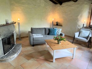A cozy living room with a fireplace, a grey sofa, a wooden coffee table, and two floor lamps. - Casa Girasol by Interhome (Cavigliano)