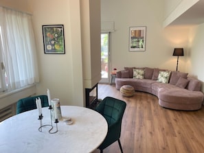 Un salon avec une table ronde, des chaises vertes, un canapé rose et deux tableaux encadrés accrochés au mur.