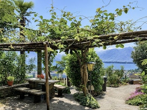 A garden with a pergola, seating, and a view of a lake. - Casa Colombina Duplex by Interhome (Gordola)