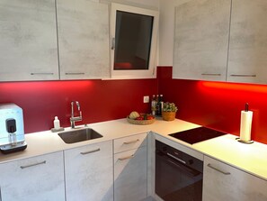 Eine kompakte Küche mit Spüle, einem Backofen und einem Fenster über der Arbeitsplatte.