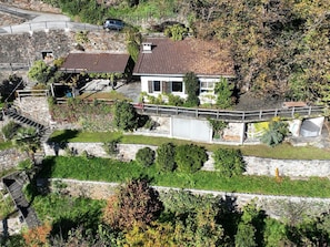 Ein zweigeschossiges Haus mit einer Steinstufe, einer überdachten Terrasse und einem Garten mit verschiedenen Pflanzen.