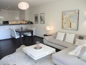 Ein modernes Wohnzimmer mit Essbereich, einer Couch, einem Couchtisch und einer Küche im Hintergrund.