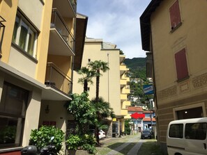 A narrow street with multi-story buildings, a parked car, and a white van. - Apartment Alice by Interhome (Locarno)