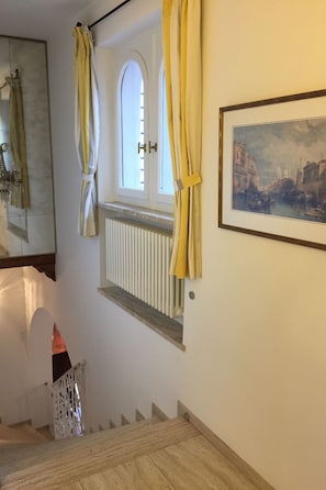 Eine Treppe mit weißer Geländer, ein Fenster mit gelben Vorhängen und ein gerahmtes Bild an der Wand.