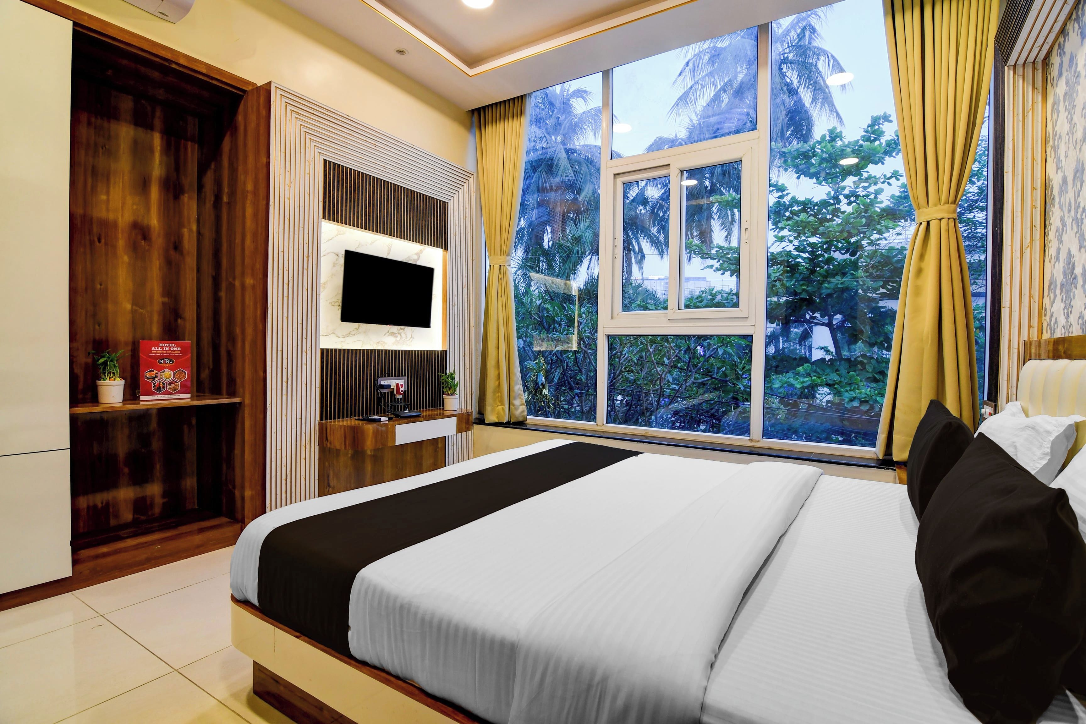 Habitación de hotel con una cama grande, televisor montado en la pared, escritorio con computadora y ventana con cortinas.
