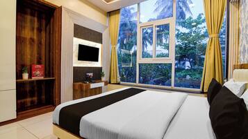 Habitación de hotel con una cama grande, televisor montado en la pared, escritorio con computadora y ventana con cortinas.