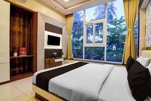 Habitación de hotel con una cama grande, televisor montado en la pared, escritorio con computadora y ventana con cortinas.