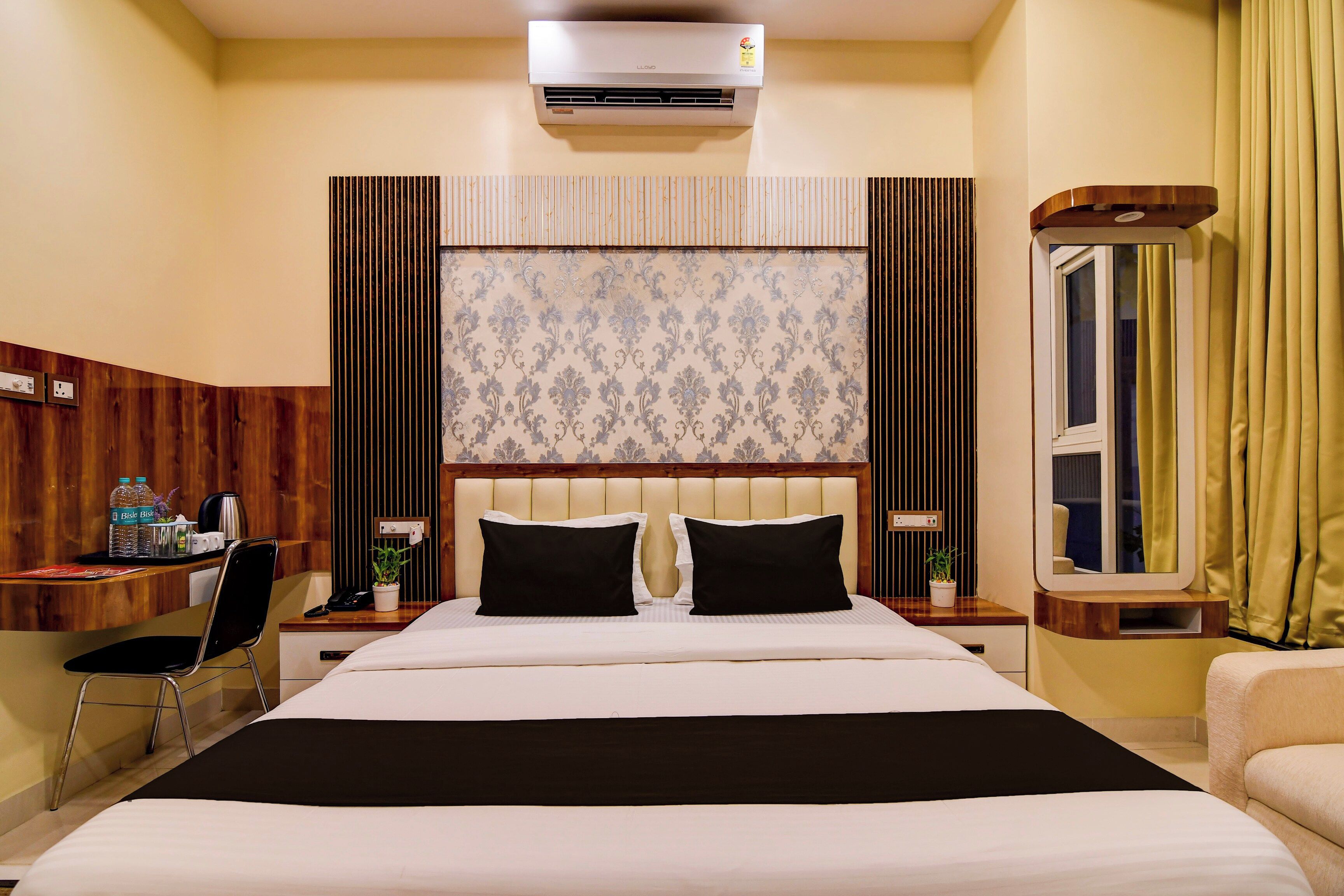 Habitación de hotel con cama, mesitas de noche, un escritorio, una silla, una planta en maceta y una ventana con cortinas.