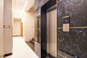 An elevator with a digital display, marble walls, and a corridor with a light-colored floor. - Super Townhouse Hotel All In One  (Barasat)