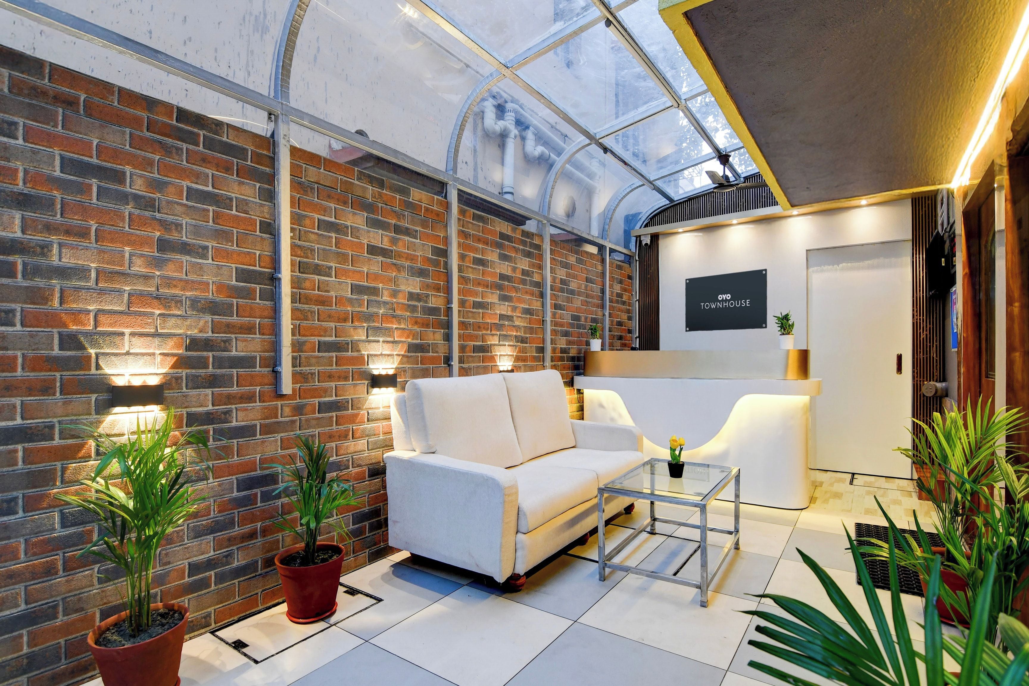 Un interior moderno con pared de ladrillo, un sofá blanco, una mesa de centro de vidrio y plantas en macetas.