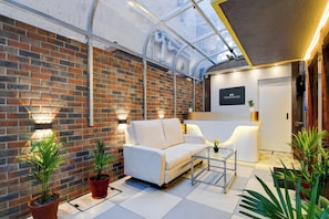 A modern interior with a brick wall, a white sofa, a glass coffee table, and potted plants. - Super Townhouse Hotel All In One  (Barasat)