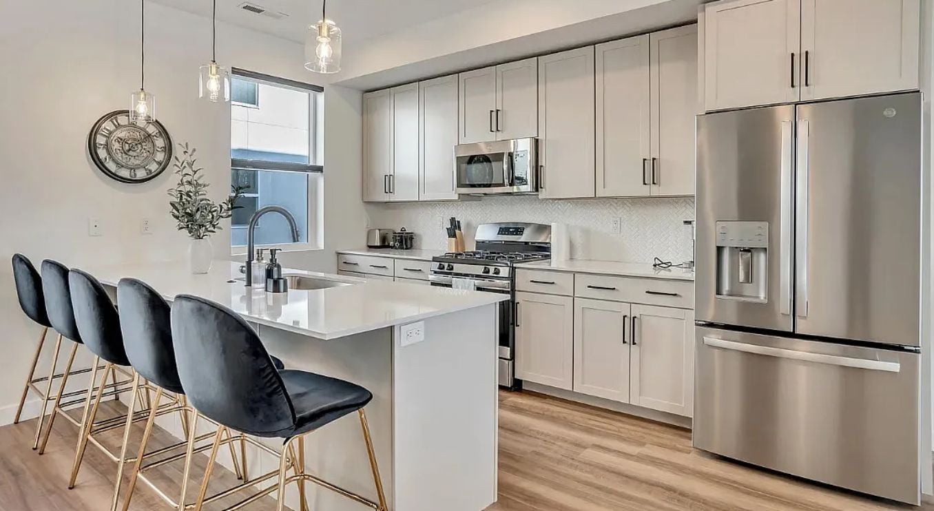 A modern kitchen with a central island, stainless steel appliances, and a dining area with bar stools.