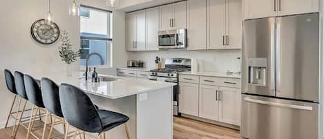 A modern kitchen with a central island, stainless steel appliances, and a dining area with bar stools.