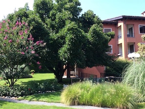 A building with a red facade, a well-maintained garden with various plants, and a clear sky. - Residenza Sabrina Duplex by Interhome (Ascona)