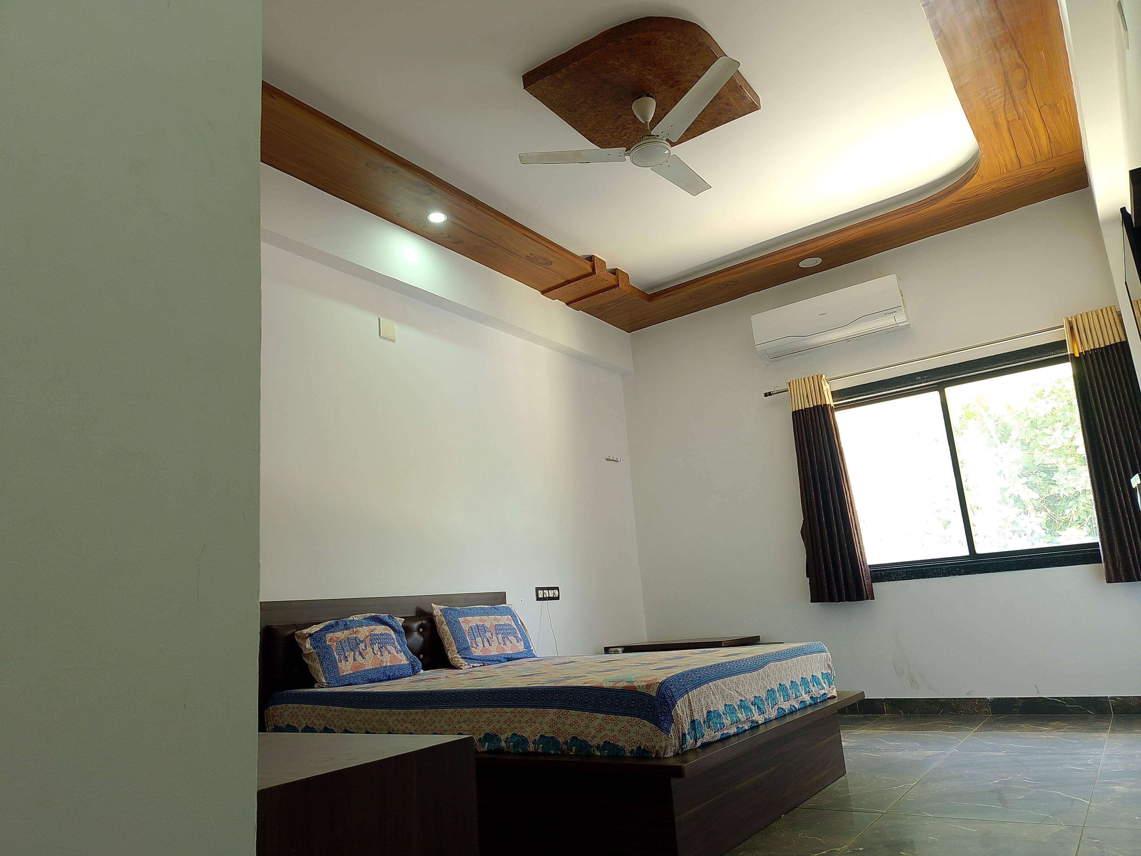A bedroom with a bed, a ceiling fan, an air conditioning unit, and a window with curtains.