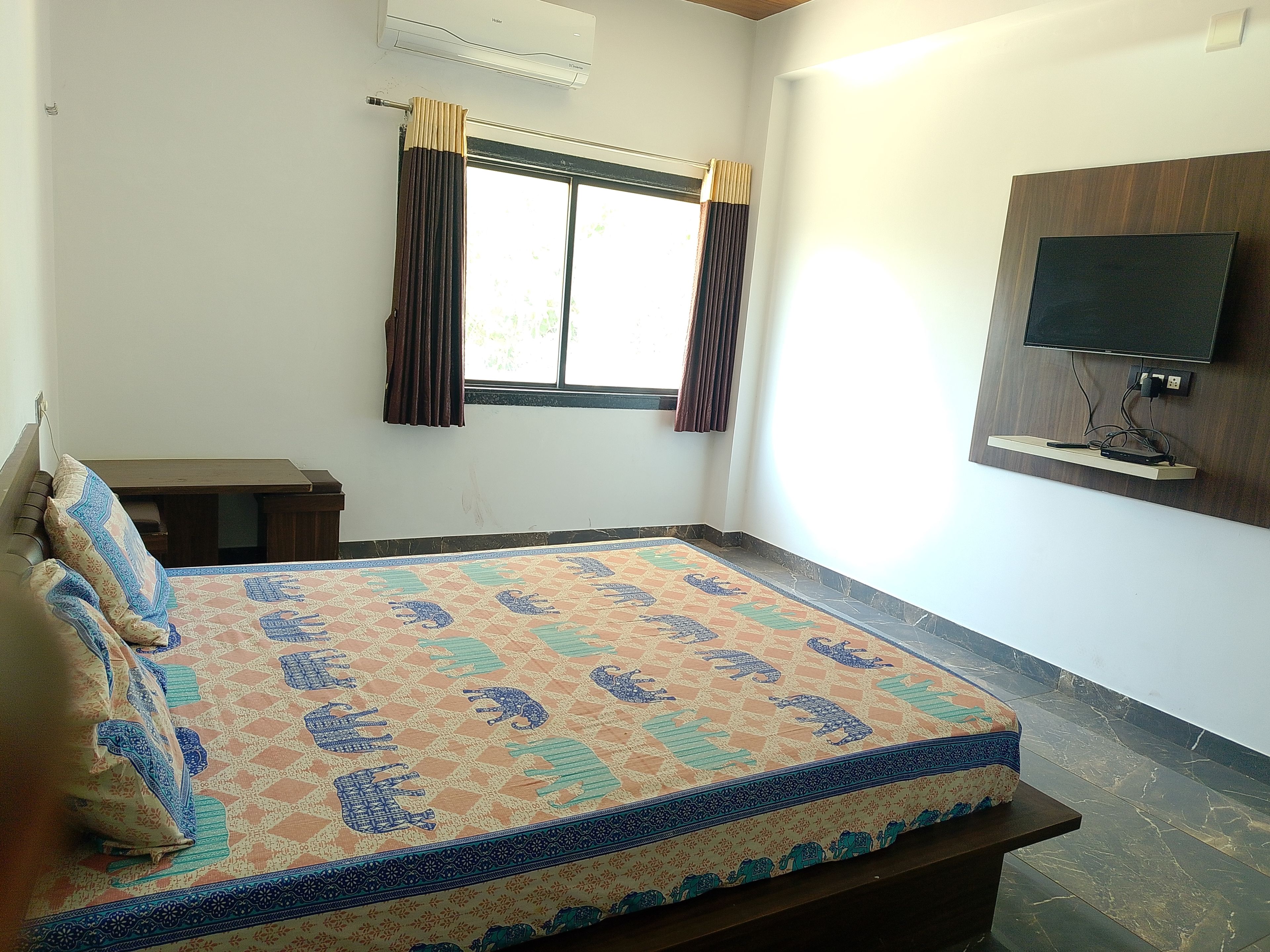 Un dormitorio con cama, televisión montada en la pared, ventana con cortinas y ventilador de techo.