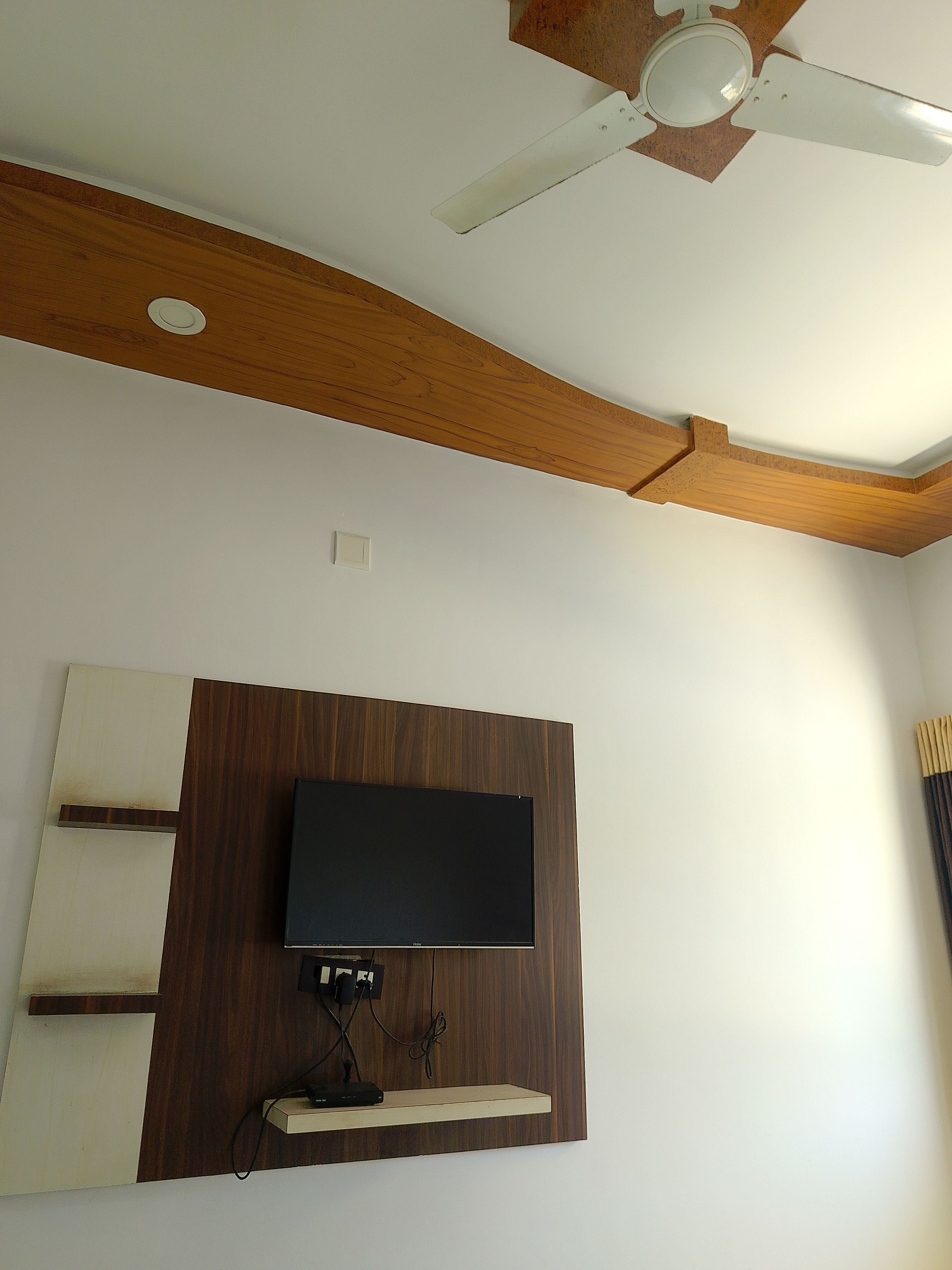 Une pièce dotée d’un ventilateur de plafond, d’un téléviseur à écran plat fixé au mur et d’un plafond avec des poutres apparentes.