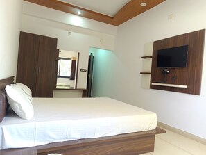 A bedroom with a bed, wardrobe, mirror, and a mounted TV. - Hotel Jai Hind (Udaipur)