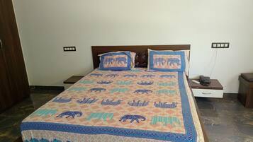 Un lit avec une couvre-lit à motifs, deux oreillers, une table de chevet avec un téléphone et une petite table de nuit avec une lampe.
