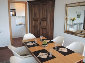 Uma sala de jantar com uma mesa de madeira posta para quatro pessoas, cadeiras brancas e um espelho grande na parede.