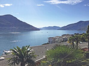 Vista sulla costa con un lago tranquillo, montagne sullo sfondo e un edificio con area piscina in primo piano.