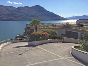 Uma área de estacionamento com design curvilíneo, rodeada por edifícios com varandas com vista para um lago e montanhas.